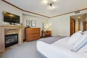 Bedroom featuring a fireplace with flush hearth, crown molding, and carpet floors
