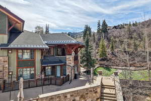 View of front of property with roof with shingles, board and batten siding, a patio area, stone siding, and a balcony