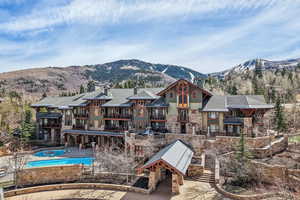 Back of house featuring a mountain view, stone siding, a chimney, and a patio area