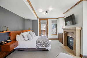 Bedroom with a premium fireplace, light colored carpet, access to exterior, and ornamental molding