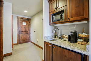 Kitchen with light stone countertops, light carpet, black microwave, a textured ceiling, and recessed lighting