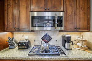 Kitchen featuring stainless steel appliances, decorative backsplash, and light stone countertops