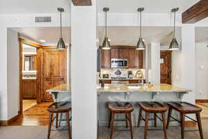 Kitchen with a kitchen bar, light stone counters, decorative backsplash, and hanging light fixtures