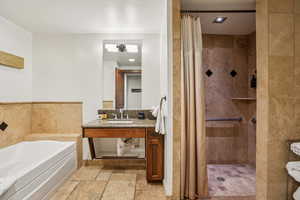 Bathroom featuring stone tile floors, a shower stall, vanity, and a bath