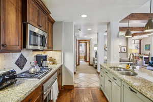 Kitchen featuring open floor plan, stainless steel appliances, light stone countertops, beamed ceiling, and dark wood finished floors