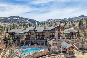 Back of house with a mountain view, stone siding, an outdoor pool, and a chimney