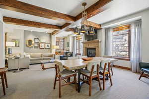 Dining space with beam ceiling, healthy amount of natural light, light colored carpet, and a glass covered fireplace