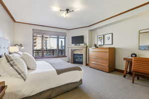 Bedroom with light colored carpet, a glass covered fireplace, and crown molding