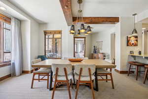 Dining room with light carpet, plenty of natural light, beam ceiling, and a chandelier