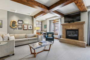 Living area with beamed ceiling, carpet flooring, and a glass covered fireplace