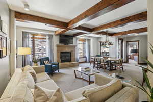 Living area featuring carpet flooring, a glass covered fireplace, and beamed ceiling