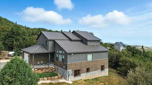 Rear view of property with brick siding, a patio area, a metal roof, and an attached garage
