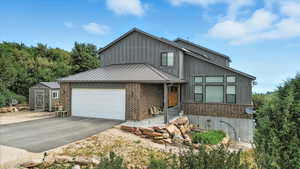 View of front of home with asphalt driveway, board and batten siding, brick siding, a garage, and a shed