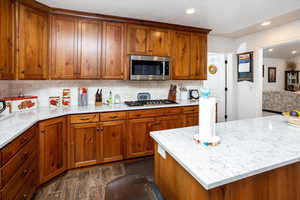 Kitchen featuring wood finish cabinetry, wood finish floors, stainless steel appliances, light stone counters, and recessed lighting