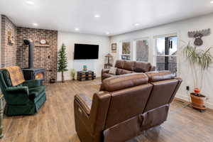 Living area with wood finish floors, a wood stove, recessed lighting, and brick wall