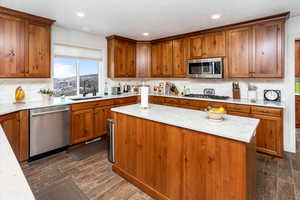 Kitchen featuring wood finish cabinetry, wood finish floors, stainless steel appliances, a center island, and decorative backsplash