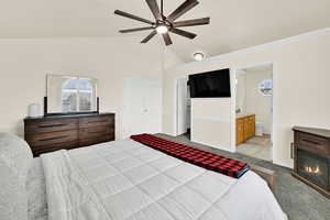 Bedroom featuring dark colored carpet, ceiling fan, vaulted ceiling, a closet, and a glass covered fireplace