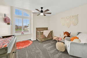 Bedroom featuring a crib, dark carpet, and a ceiling fan
