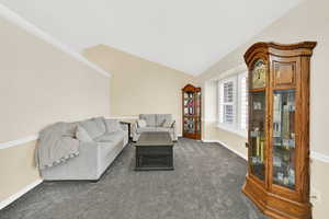 Carpeted living area featuring baseboards and lofted ceiling