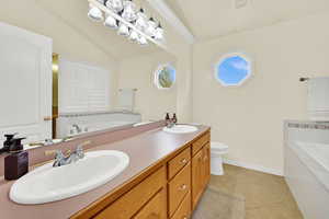 Bathroom featuring a bath, double vanity, light tile patterned floors, and vaulted ceiling