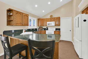 Kitchen with dark countertops, white appliances, wood finish cabinets, a breakfast bar, and lofted ceiling