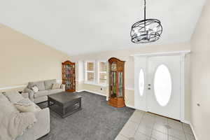 Entryway with light colored carpet, light tile patterned flooring, hanging lights, and lofted ceiling