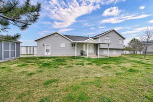 Back of property with a yard, a patio area, a storage unit, and roof with shingles