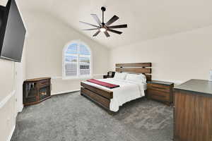 Bedroom featuring dark colored carpet, a ceiling fan, vaulted ceiling, and a glass covered fireplace