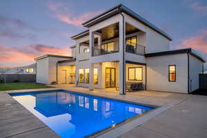 Back of house at dusk featuring a patio, a balcony, stucco siding, and ceiling fan