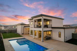 Back of house at dusk featuring a patio, stucco siding, a fenced backyard, a balcony, and an outdoor living space