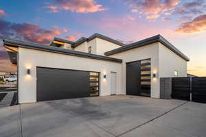 Contemporary home featuring an attached garage, concrete driveway, stucco siding, and a gate