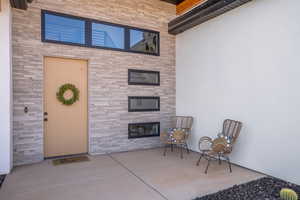 Doorway to property with stone siding, a patio, stucco siding, and a glass covered fireplace