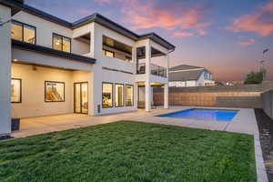 Back of house at dusk featuring a balcony, stucco siding, a patio, and a fenced backyard