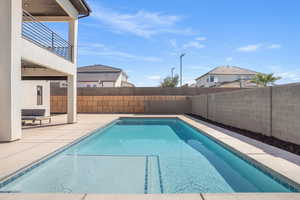 View of pool featuring a fenced backyard, patio surround, and a balcony