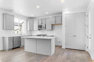 Modern kitchen featuring light gray cabinetry, stainless steel appliances, a white subway tile backsplash, and light wood-finish flooring