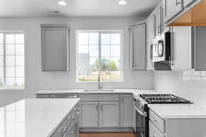 Modern kitchen featuring white subway tile backsplash, light grey cabinetry with brushed nickel hardware, and light-toned countertops