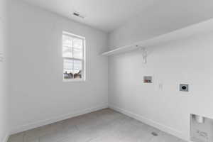 Utility room featuring a double-hung window, light-toned tile flooring, white walls, and an overhead shelf