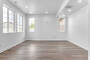 Spacious interior room featuring multiple grid-pattern windows, recessed lighting, wood-finish flooring, and crisp white walls with matching baseboards