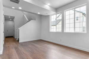 Spacious room featuring wood-finish flooring, two large grid-pattern windows, recessed lighting, and a contemporary staircase with white balusters