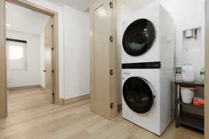 Laundry area with light wood finished floors, stacked washer / dryer, and recessed lighting