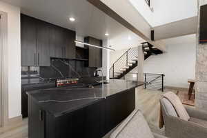 Kitchen featuring light wood-style floors, modern cabinets, a kitchen island with sink, quartz counter tops, tasteful backsplash, and decorative light fixtures