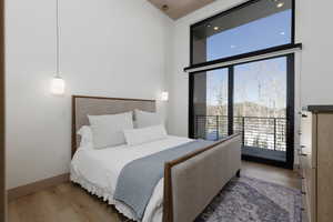 Bedroom with wood finished floors, built in dressers, private balcony facing ski resort, expansive windows, and a high ceiling