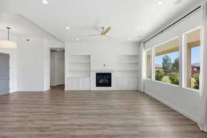 Unfurnished living room with light wood-style flooring, a ceiling fan, a glass covered fireplace, built in features, and recessed lighting