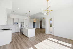 Kitchen featuring open floor plan, an island with sink, white cabinetry, light wood-style floors, and ceiling fan