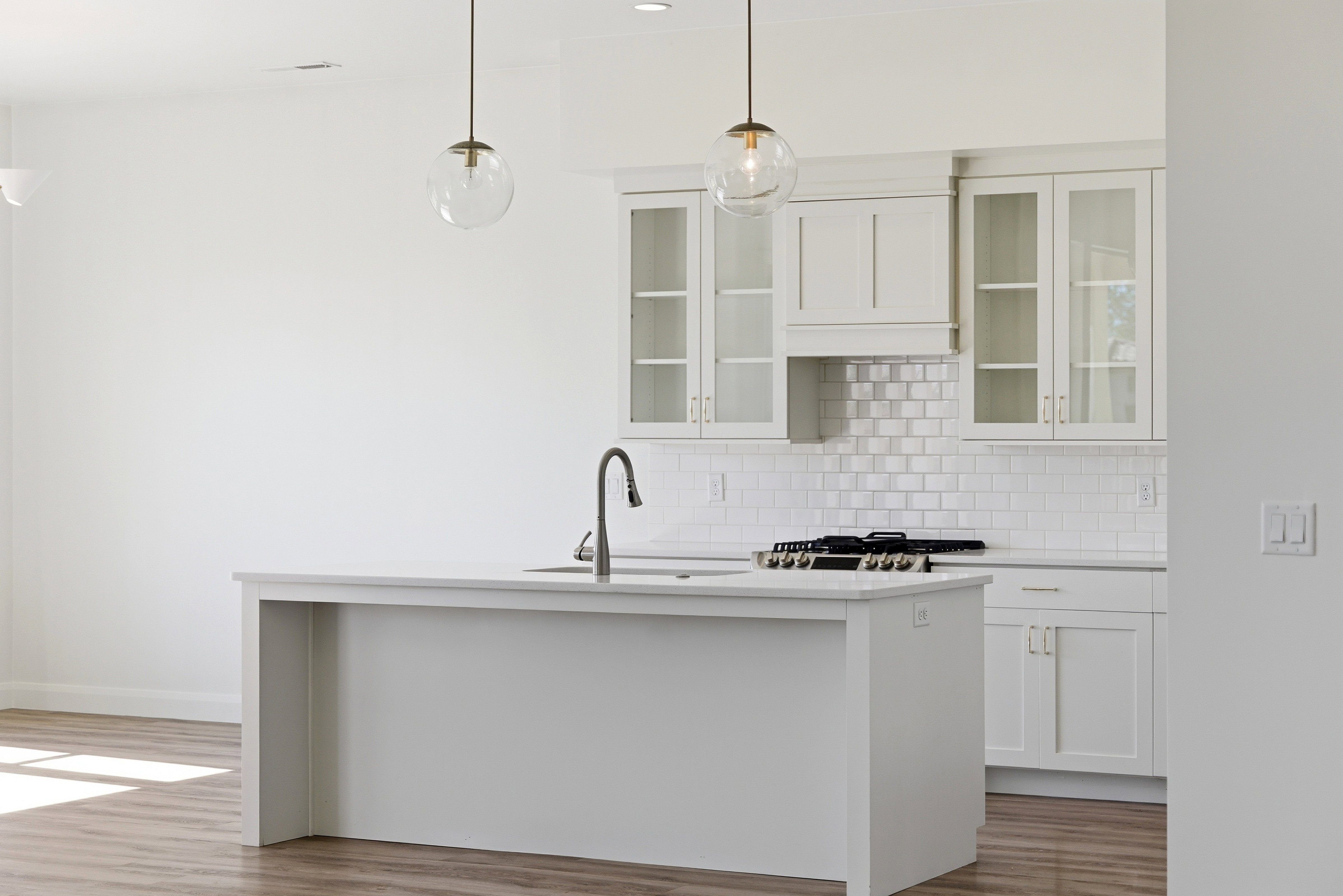 Kitchen featuring white cabinetry, hanging light fixtures, glass fronted cabinets, tasteful backsplash, and a center island with sink