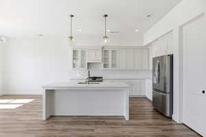 Kitchen featuring stainless steel appliances, glass insert cabinets, a kitchen island with sink, white cabinetry, and light wood-style flooring