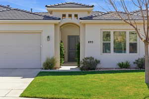 View of front of house with an attached garage, stucco siding, a front lawn, and a tile roof
