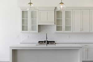 Kitchen featuring white cabinetry, glass insert cabinets, light stone counters, and pendant lighting