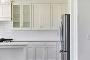 Kitchen with glass fronted cabinets, stainless steel appliances, tasteful backsplash, and white cabinets
