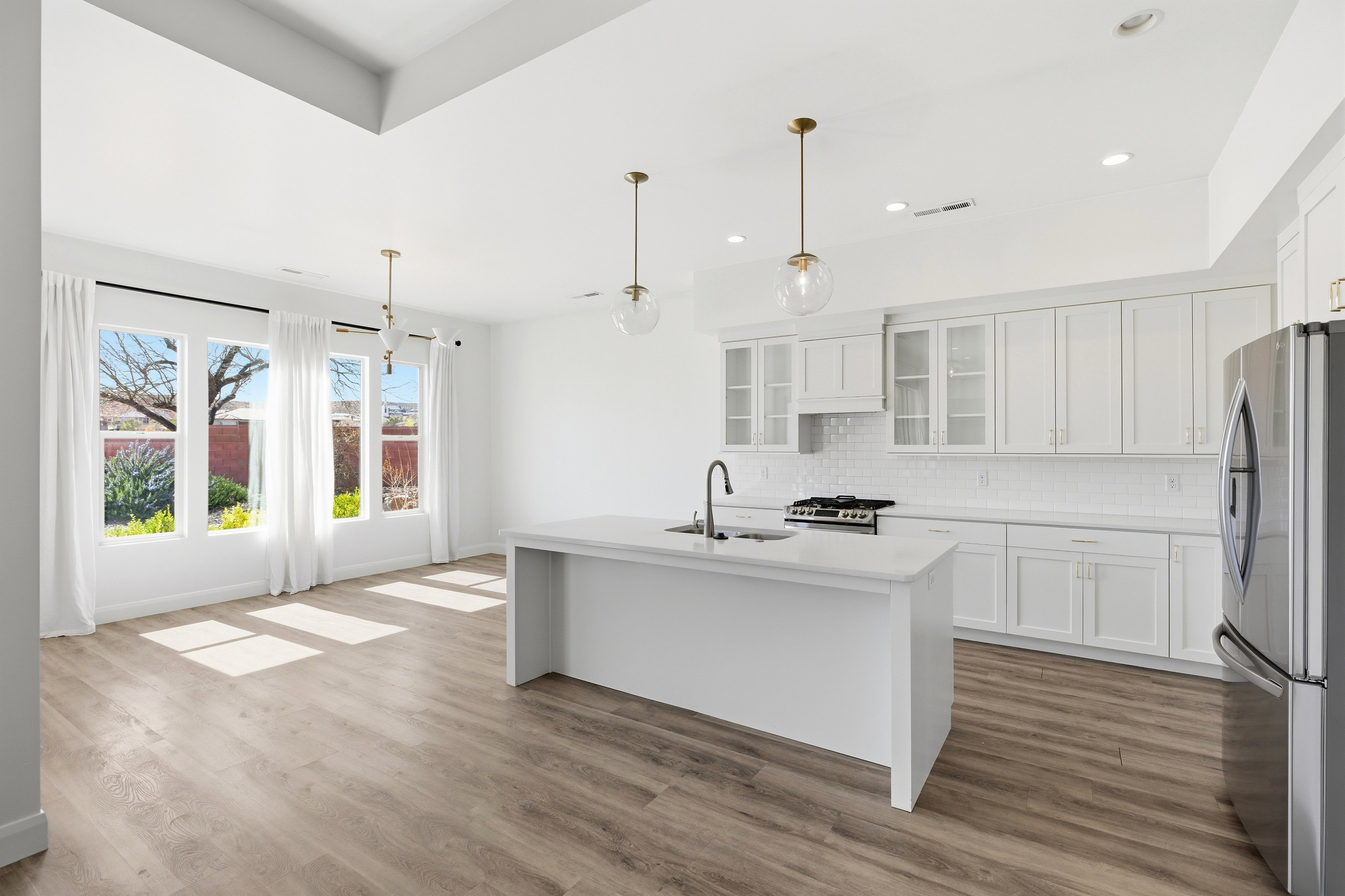 Kitchen with stainless steel appliances, white cabinetry, glass fronted cabinets, a center island with sink, and decorative light fixtures